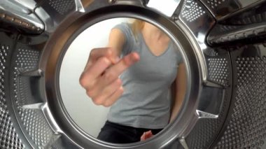 chamber is inside drum of washing machine. woman's hand shows fig and an obscene gesture, fuck you. woman puts her hand inside and shows that she is tired of doing laundry and cleaning. wants to rest