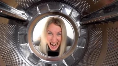 Genç güzel sarışın kadın kafasını gizlice çamaşır makinesine sokuyor. Öfkeli, çamaşır yıkamak istemiyor ve sürekli temizlik ve çamaşır yıkamaktan yorulmuş. Davulun içinden, geniş açılı kamera görüntüsü.