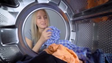 Çamaşır makinesindeki kadın eli ve temiz çamaşırlar yakın çekimdir. Çamaşır makinesinin içinden bak. Çamaşır konsepti. Kız kıyafetlerini davuldan çıkarıyor. Ev hanımı rutini, temizlik. ev işleri.