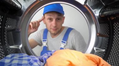 Mavi üniformalı bir ev aletleri tamircisi kafasını çamaşır makinesinin variline sokuyor ve işaret parmağını şakağına çarpıyor. Tatminsiz ve tehlike konusunda uyarıyor. Çamaşır makinelerinin tamiri.