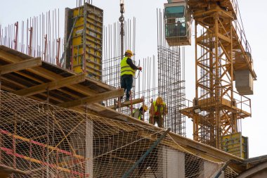 Builders in helmets, light green and yellow vests install fittings on the building. Construction concept
