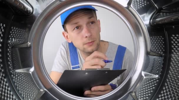 Junger Waschmaschinenmechaniker Blickt Auf Trommel Und Schreibt Werkliste Tablet Mit — Stockvideo