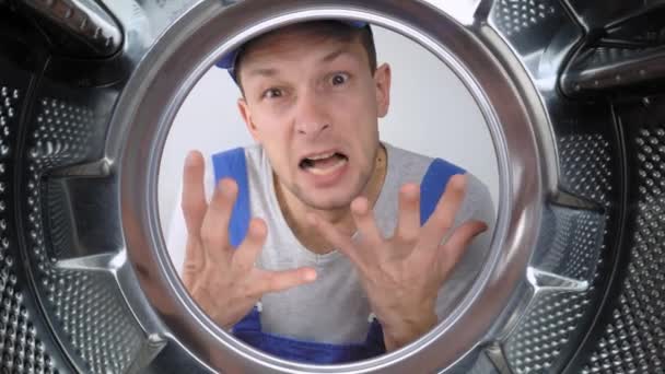 一个穿着蓝色制服的家用电器修理工把头伸进洗衣机的鼓里 从嘴里尖声尖叫着 他不满意 并警告危险 洗衣机的修理 — 图库视频影像