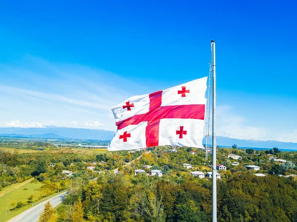 Close-up view from a drone of the Georgian flag against the background of mountains, trees on a sunny autumn day