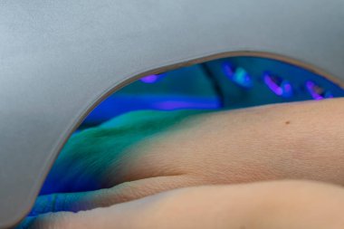 Güzellik salonunda jel cilasını kurutmak için ultraviyole lamba kullanan bir elin yakın çekimi.