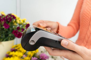 Çiçekçinin elindeki ödeme terminalinin yakın plan görüntüsü. Müşterinin eli, temassız bir kartla siparişin parasını ödüyor.