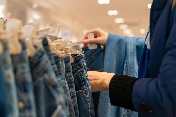 Close-up of women\'s hands choosing blue jeans at the mall. Shopping concept