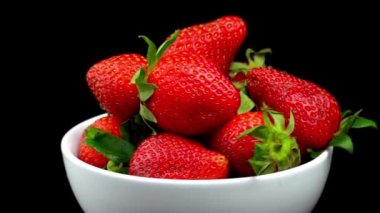 Appetizing strawberries with wilted green leaves lie on white porcelain bowl