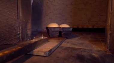 Baker places bread dough in oven with shovel.