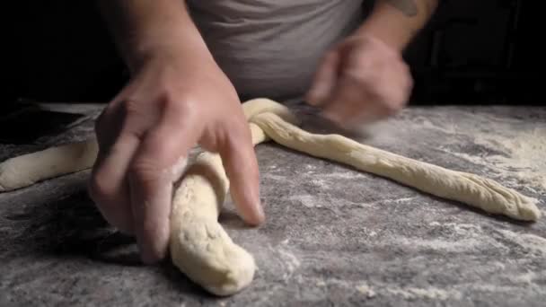 Men's hands knead dough on wooden table with flour and make braid — Video