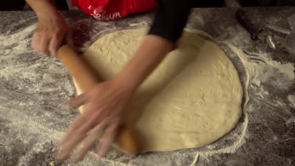 Chef rocks dough with rolling pin on kitchen table against background of flour — Stock video
