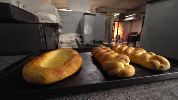 Gebakken gebak in de vorm van broodjes en brood liggen op tafel tegen achtergrond bakkerij — Stockvideo