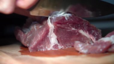 Girl's hands cut raw pork meat with knife for further cooking.