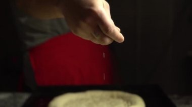 Tattooed hand pours sesame seeds or salt on bread,