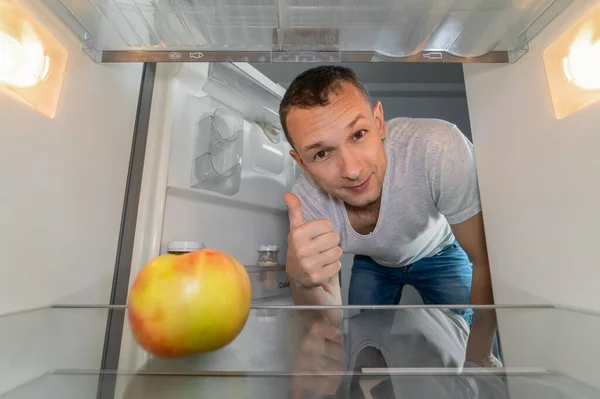 Smiling Man Looks Refrigerator One Apple Shows Thumbs Concept Healthy — Zdjęcie stockowe