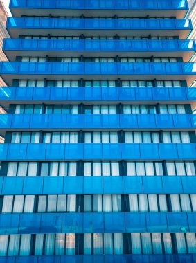 Birçok pencere ve balkonu olan modern çok katlı bir binanın insansız hava aracının yakın görüntüsü. Çok katlı, mavi cam bina, apartmanlar, otel. Dikey fotoğraf