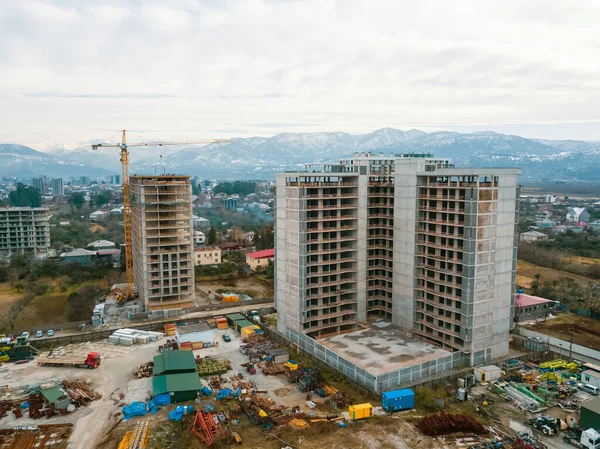 Drone view of the construction site, multi-storey buildings under construction against the background of mountains. Construction machinery, excavators, tractor crane