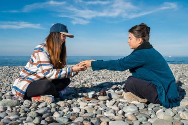 İki kadın çay seremonisine hazırlanıyor. Çaydanlık, iki fincan, güneşli bir günde çakıl taşlı sahilde çay içen bambu bir tekne.