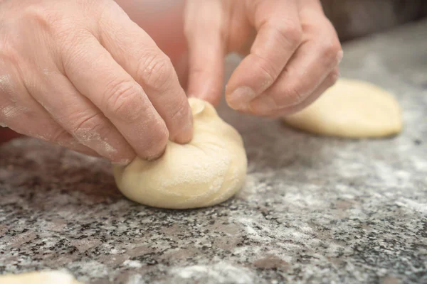 Close-up female hands of a pastry chef form buns from yeast dough on a table with flour, selective focus