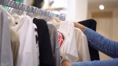 Beautiful young Caucasian woman with white hair chooses clothes in store or shopping center. She removes her clothes from hanger and inspects them. T-shirts and jeans. close-up