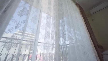 Rüzgâr odanın açık penceresinden esiyor. Dalları beyaz tül. Sabah güneşi odayı aydınlatır. Gölge arkaplanı üst üste gelir. Kamerayı pencerenin yanına, perdenin asılı olduğu kata taşı.