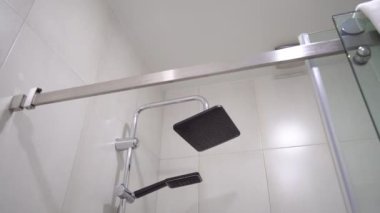 Banyoda eski gri çiçeklerle modern yenileme. Duş başlığı yağmuru. Beyaz tavan. Modern duş kabini. Yakın plan. Kamera hareketi.