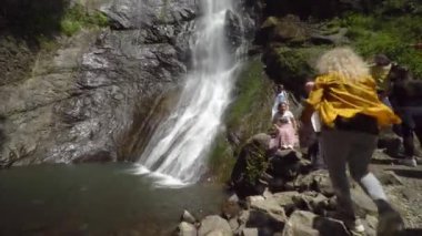 BAtumi, Georgia - May 22, 2022: Large number of random travelers sit at Mirveti Waterfall in Georgia. They sat down to rest after long journey under pouring sun and beautiful view.