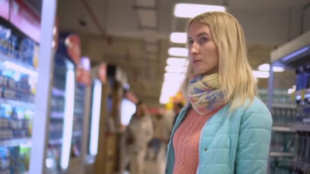 Young Blonde Businesswoman Stands Large Supermarket Row Shelf Briefly Looks — Vídeo de stock