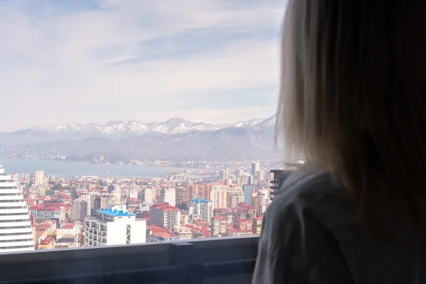 Portrait of a blonde woman from the back looking from a height at the city and mountains on a sunny day, copy space