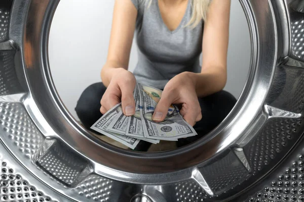 Women\'s hands hold money near the washing machine, a photo from inside the drum of the washing machine. Concept of payment, money laundering.