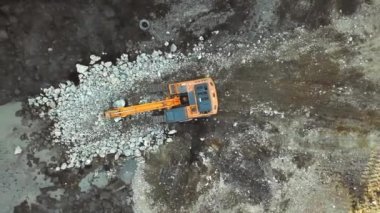 Büyük sarı kazıcı ya da buldozer taşları kovayla doldurur ve çukurları ya da suyun toplandığı su birikintilerini doldurur. İnşaat alanı. İnşaat. Ağır makineler toprağı kazıyor..