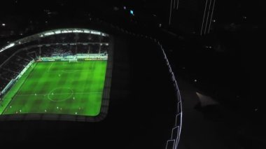 View of stadium with football field in middle of city of Batumi in Georgia. visible from above at night with stadium lights on and athletes playing football. Drone flight around playground altitude.