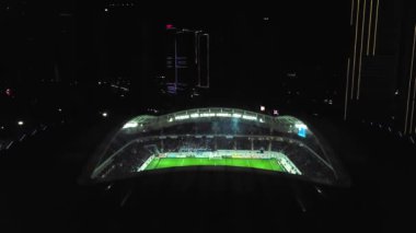 View of stadium with football field in middle of city of Batumi in Georgia. visible from above at night with stadium lights on and athletes playing football. Drone flight around playground altitude.