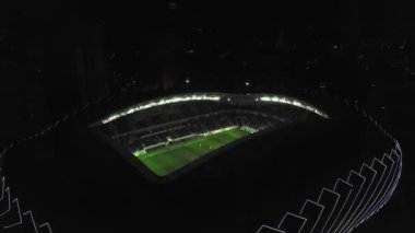 View of stadium with football field in middle of city of Batumi in Georgia. visible from above at night with stadium lights on and athletes playing football. Drone flight around playground altitude.