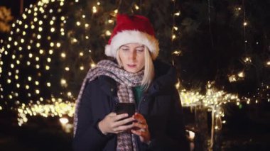 Noel Baba şapkalı güzel bir sarışının portresi, cep telefonuna mesaj yazıyor ve iyi haber alınca duygusal tepki veriyor. Şehir ışıklarının arka planındaki akıllı telefonlara bakar..