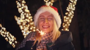 Parktaki sokak lambalarından gelen sihirli sıcak ışık Noel Baba şapkalı bir kadının gözlerine düşer. Yetişkin bir beyaz kız gözlerini kapadı ve bir dilek diliyor ya da rüya görüyor. Elimde maytaplar var..