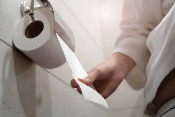 Woman in a white coat sits on the toilet and pulls toilet paper in the bathroom. Selective focus