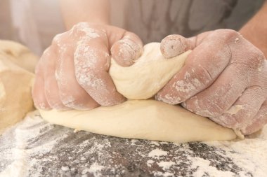 Masaya un serpiştirilmiş elastik hamur yoğuran erkek ellerine yakın plan.