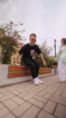 Mutlu arkadaş grubu koşar, sonra kenarda oturur ya da kenarda oturur ve konuşur. Gülüyorlar, sohbet ediyorlar ve eğleniyorlar. Oda, scooter veya elektrikli scooter 'dan uzaklaşır. Dikey video.