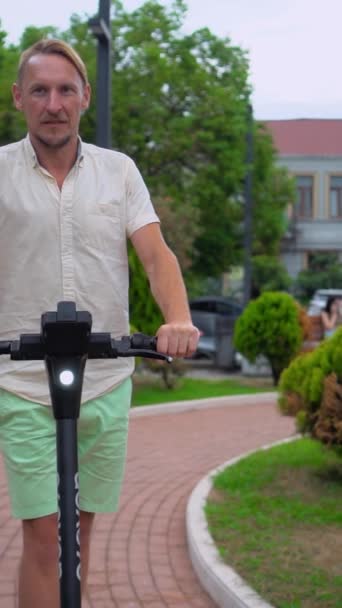 Hombre Joven Camisa Blanca Pantalones Cortos Verdes Monta Scooter Eléctrico — Vídeos de Stock