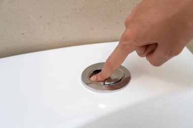 Woman's hand presses a button on a white toilet to flush