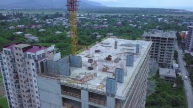 Drone view of a multi-storey building under construction with a tower crane against the background of mountains on a summer day