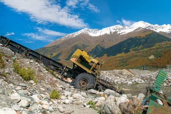 An abandoned, half-dismantled truck near a mountain river against the background of mountains on a sunny day