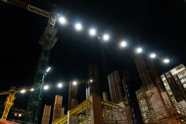 Illuminated construction cranes at night on the construction site.