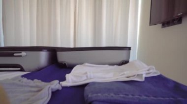 smiling young beautiful girl is talking on phone in Santa hat. She is going to a resort or vacation. A suitcase and things are lying on the bed. Christmas trip. A hotel or a room in an apartment.