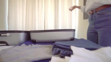 woman in Santa Claus hat collects things in suitcase after vacation or before vacation and dances and jumps to music. With smile on her face, she is going to rest. Apartment or hotel room. Christmas