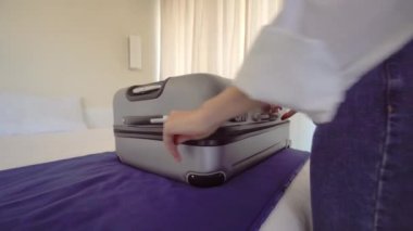 A young beautiful woman in a Santa Claus hat puts things out of a suitcase after a vacation or before a vacation. With a smile on her face, she is going to rest. Apartment or hotel room. Christmas.