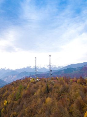 Drone view of two high-voltage towers with antennas in the forest in the mountains on an autumn day. Vertical photo