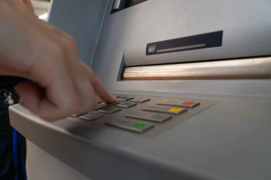 Woman's hand is typing a PIN code on the keyboard of a modern ATM in a shopping center. Selective focus