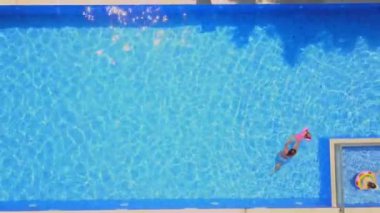Young mother swims in pool with her child. View from drone in pool in villa, mother teaches her young son to swim and dive in pool. Happy child swims in pool in summer with his mother.